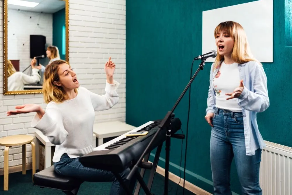 Profesora de canto acompañando con teclado a una alumna que canta al micrófono