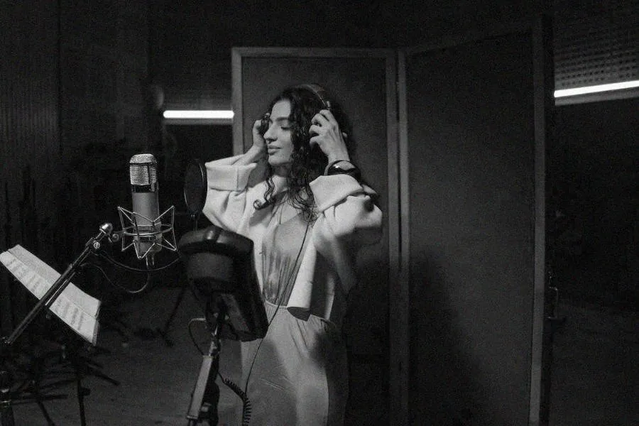 Cantante ajustándose los audífonos frente al micrófono en un estudio, en blanco y negro