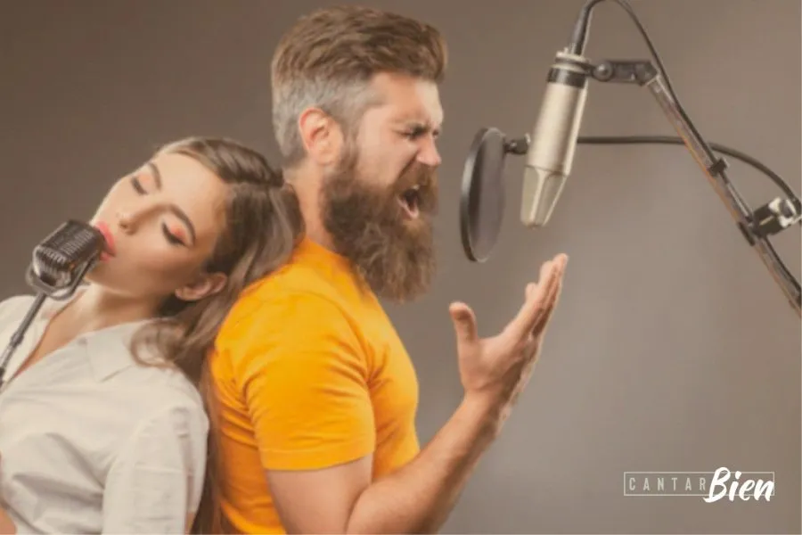 Dos cantantes espalda con espalda grabando frente a micrófonos de estudio