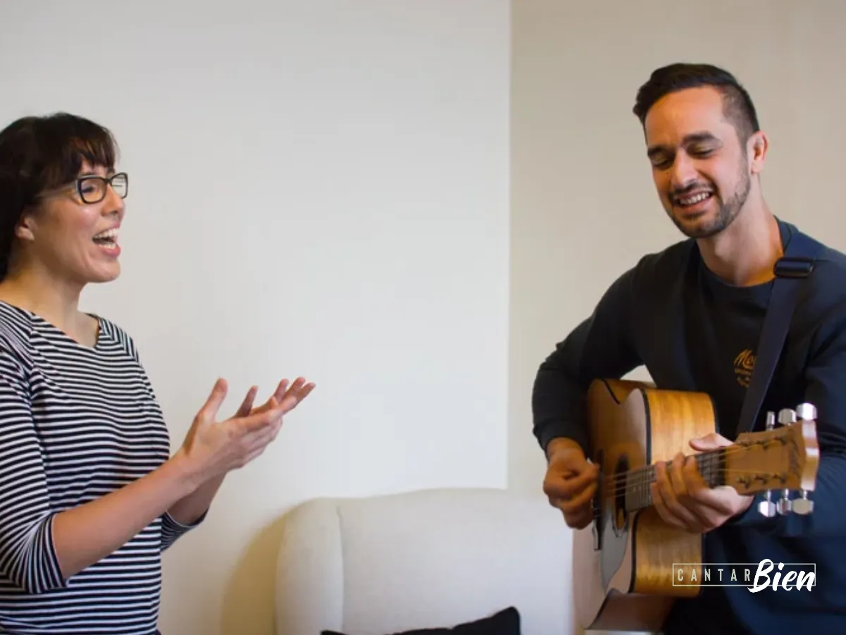 Dos músicos ensayando: ella canta mientras él acompaña con guitarra acústica
