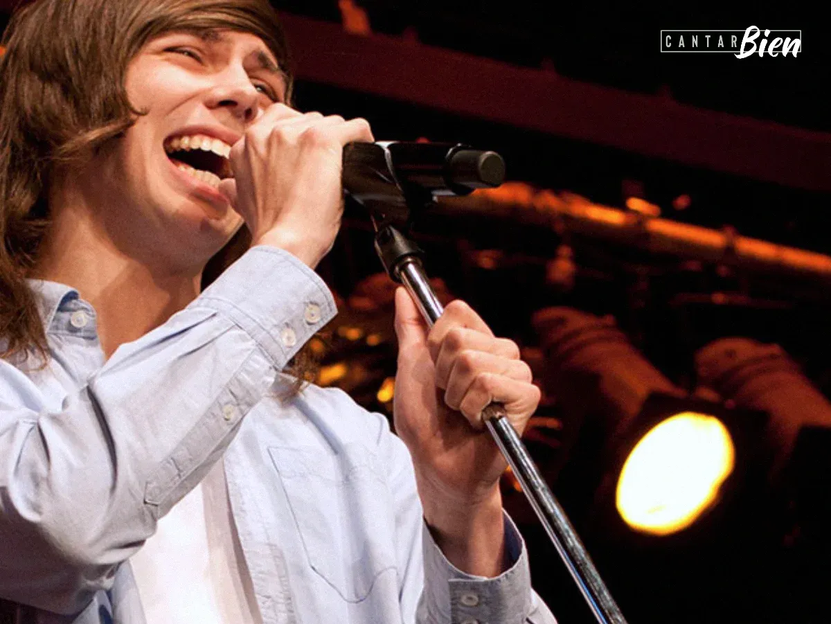 Cantante joven sonriendo mientras canta al micrófono en un escenario