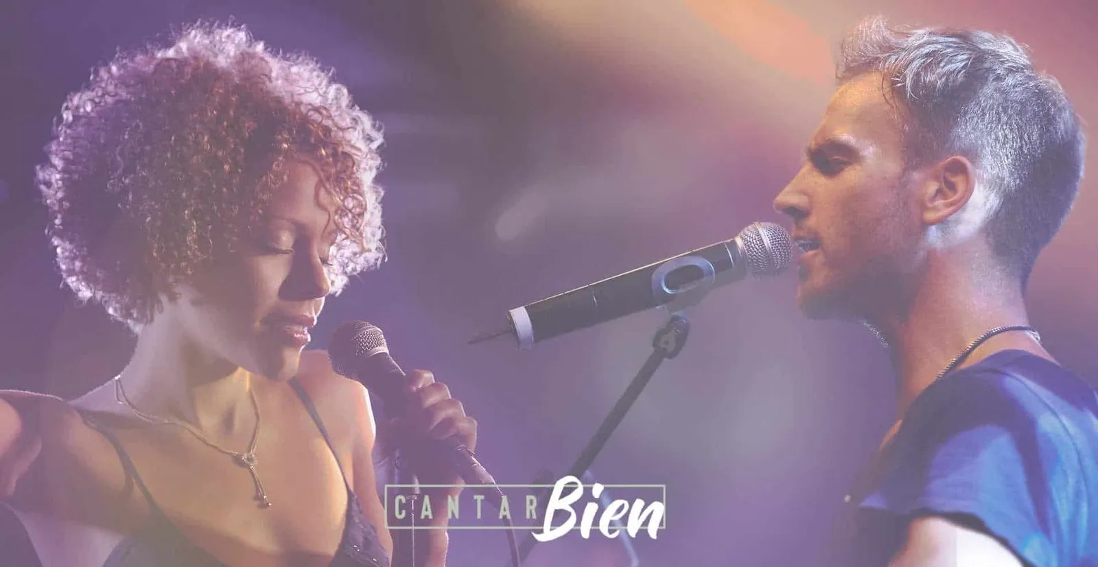 Dos cantantes frente a frente cantando con micrófonos en un escenario con luces moradas